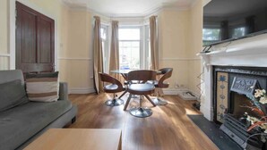 A living room with a sofa, a dining table with chairs, a fireplace, and a bay window with curtains. - Sleeps 10 few minutes' walk to Abbeywood Station (Gillingham)