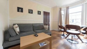 A living room with a grey sofa, a wooden coffee table, and a dining area with a round table and chairs. - Sleeps 10 few minutes' walk to Abbeywood Station (Gillingham)