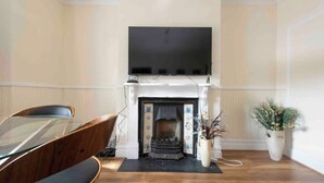 A room with a fireplace, a television mounted above it, a dining table with chairs, and a potted plant. - Sleeps 10 few minutes' walk to Abbeywood Station (Gillingham)