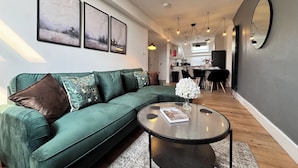 A modern living room with a green sofa, a round coffee table, and a dining area in the background. - 2 Bedroom Queen Street (Newcastle-upon-Tyne)