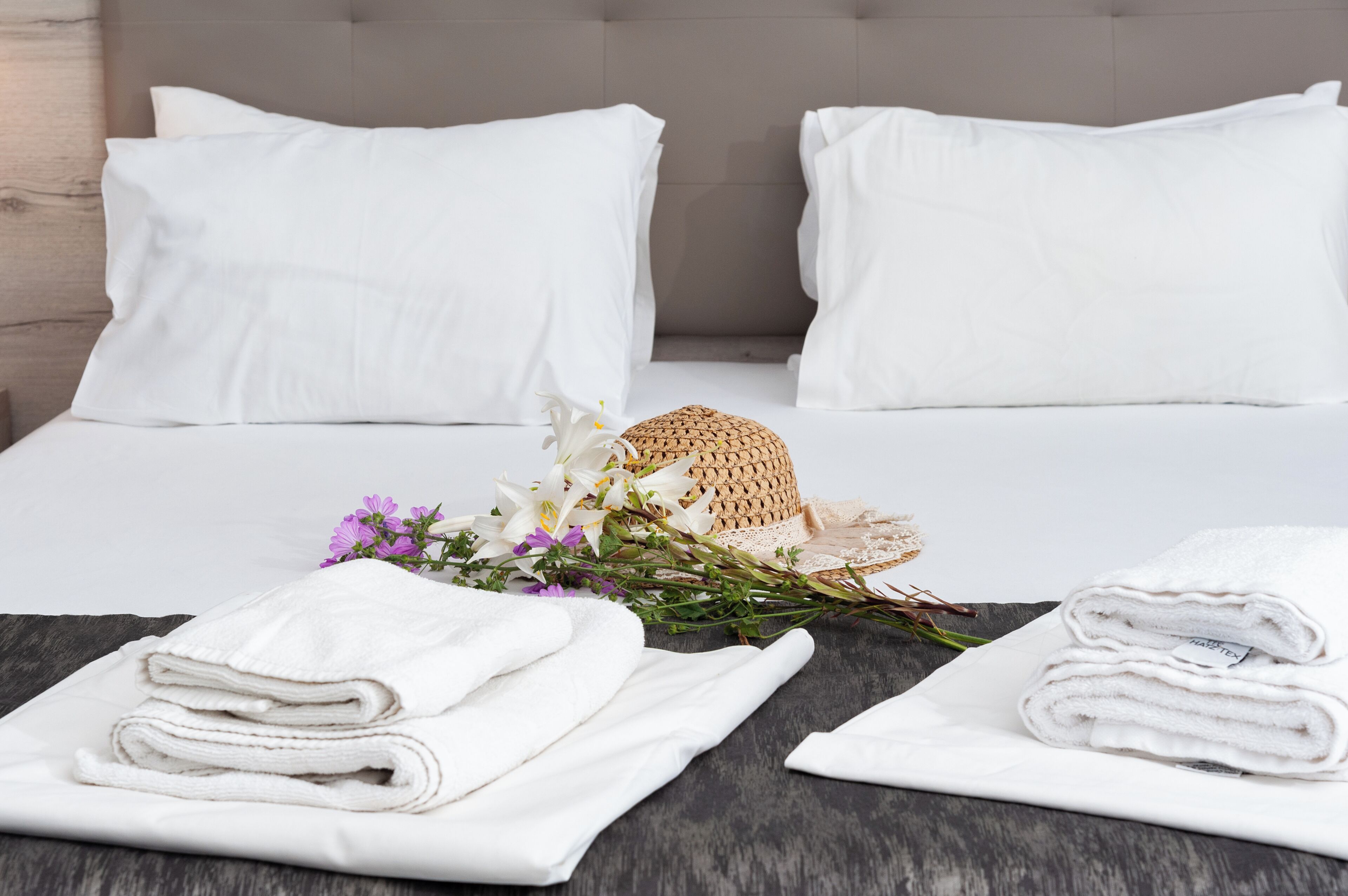 Un lit bien fait, avec du linge de lit blanc et des oreillers, un panier en osier et un bouquet de fleurs.