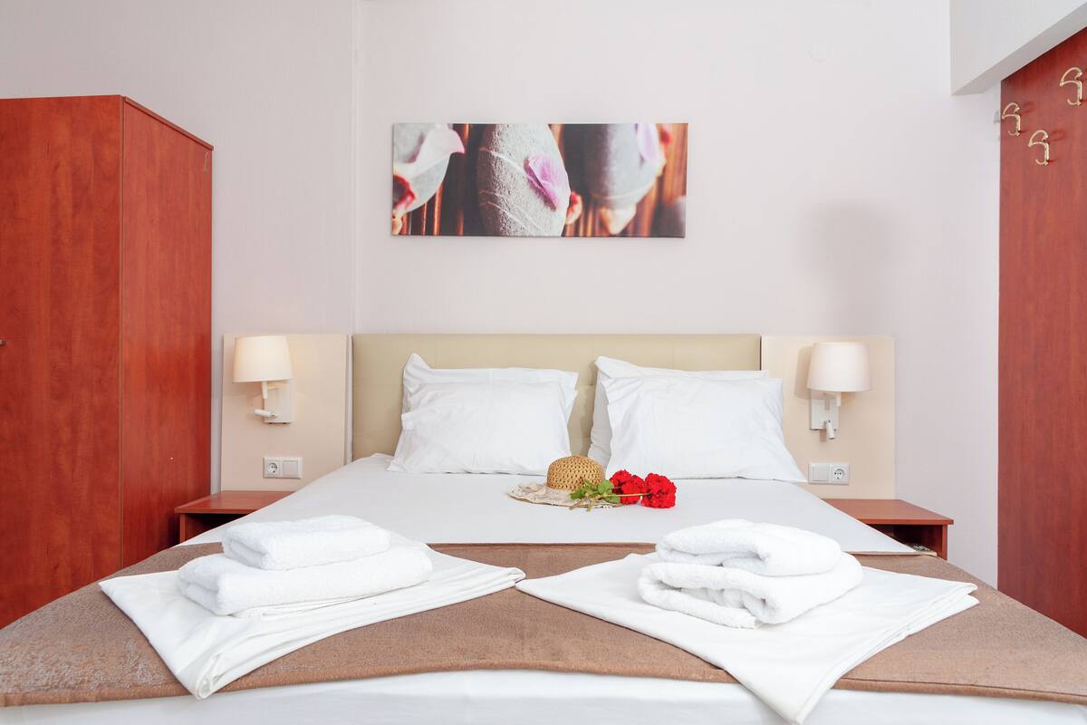 A neatly made bed with white linens, two pillows, and a decorative item on the headboard.
