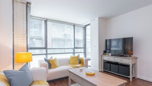 A modern living room with a sofa, a coffee table, a TV, and a lamp. - 2-bedroom apartment in charming Smithfield Market with Parking (Dublin)