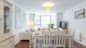 A modern kitchen with a dining area, featuring a wooden table, chairs, and a large window with blinds. - 2-bedroom apartment in charming Smithfield Market with Parking (Dublin)