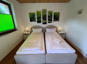 Habitación doble con dos camas, mesitas de noche con lámparas y un amplio ventanal con persianas.