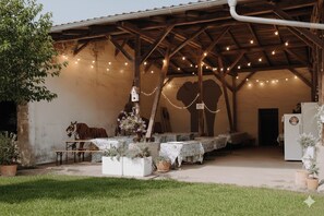 An outdoor covered patio with string lights, tables, and potted plants. - A compact and affordable vacation rental on a rural estate surrounded by nature, near a lake (Kehnert)