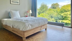 A bedroom with a large window, a bed, a bedside table with a lamp, and a framed picture on the wall. - FOUR SEASONS HOUSE (Doudeville)