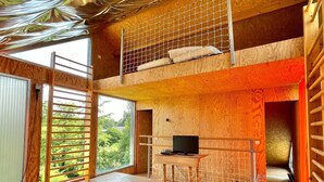 A multi-level wooden interior with a TV on a desk, a window with a view of greenery, and a red mat on the floor. - FOUR SEASONS HOUSE (Doudeville)
