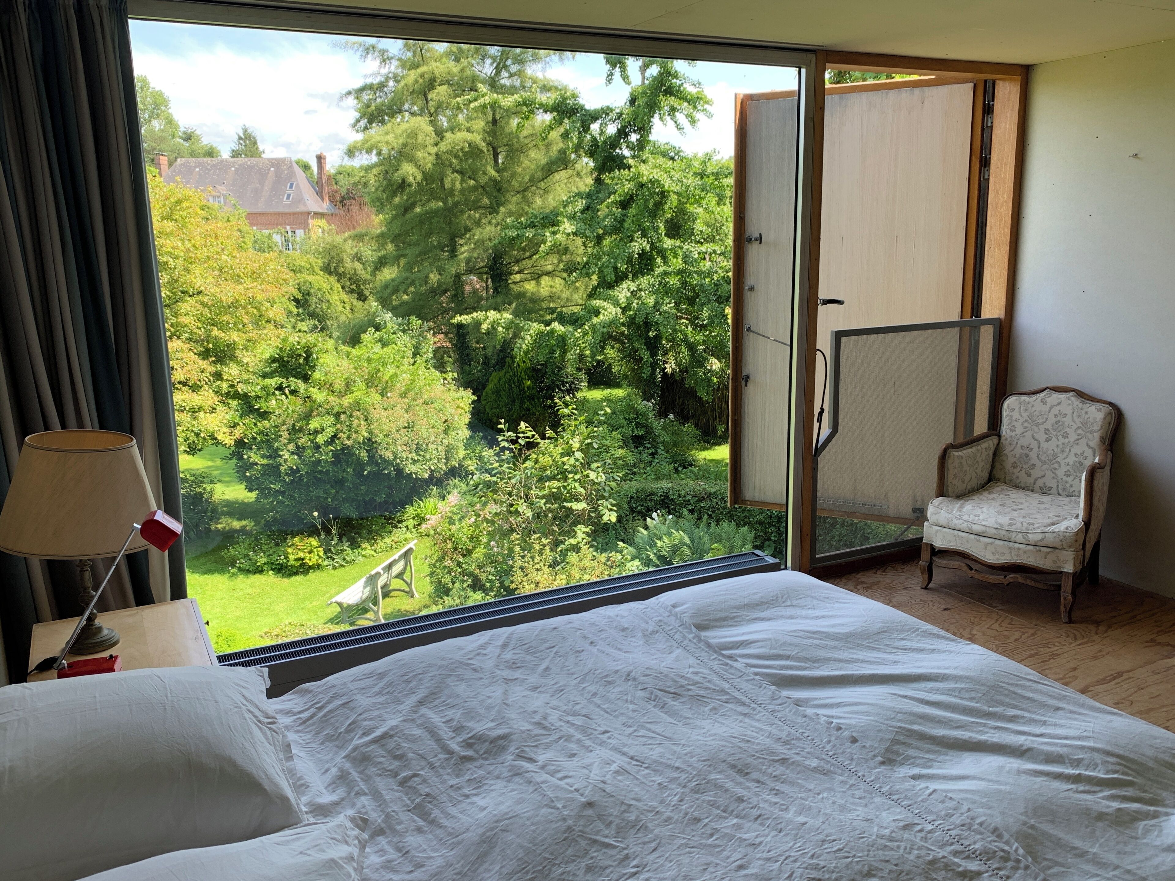 Een slaapkamer met een groot raam, een bed, een stoel en een lamp.