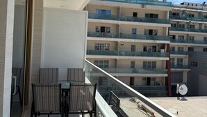 Un balcon avec une table et des chaises, donnant sur un immeuble à plusieurs étages également doté de balcons.