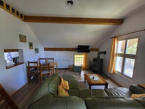 Ein gemütliches Wohnzimmer mit einem grünen Sofa, einem Holzespeisetisch und einem an der Wand montierten Fernseher.