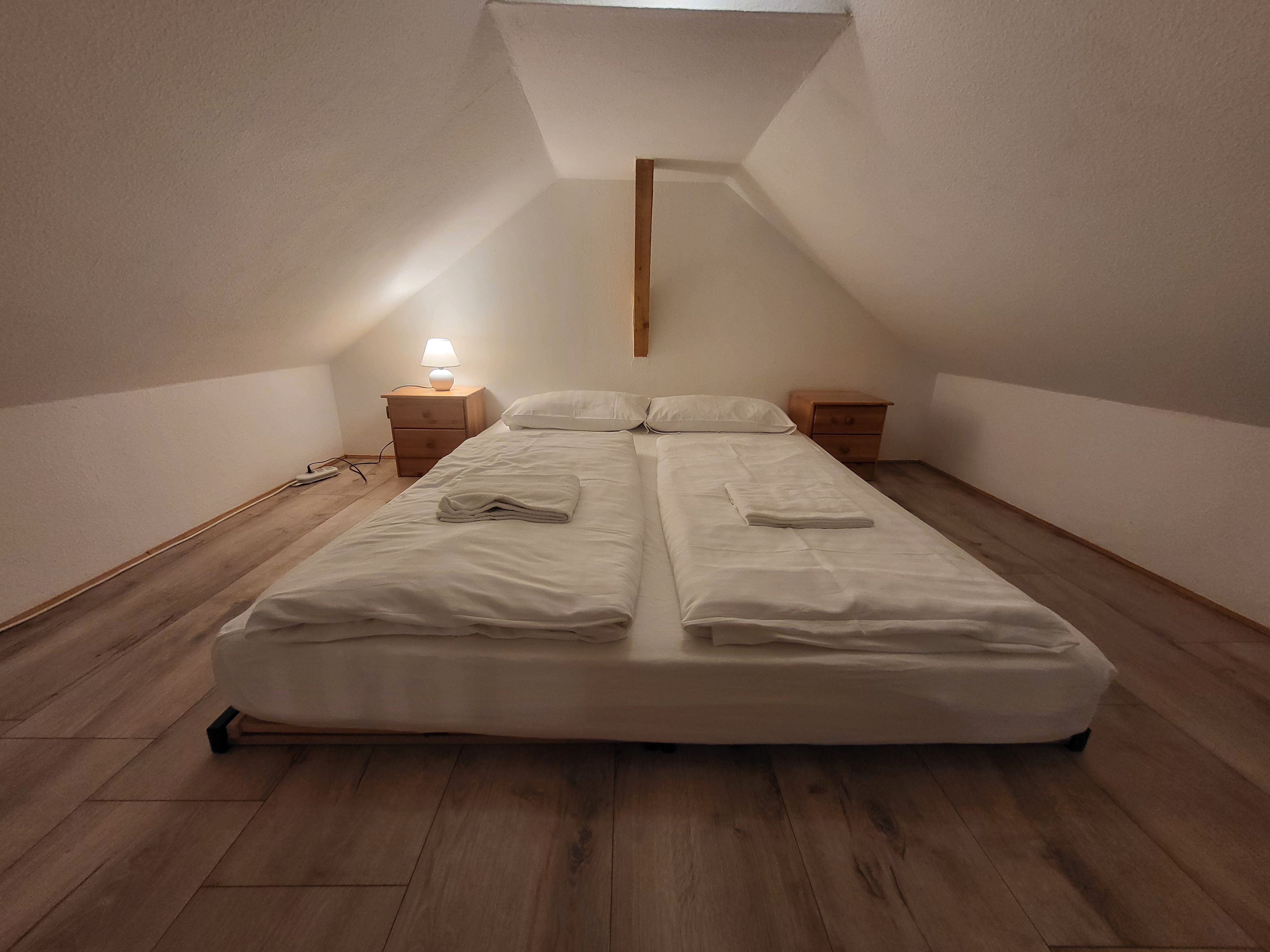 Un lit simple avec une tête de lit en bois, dans une pièce dont le plafond est en pente.
