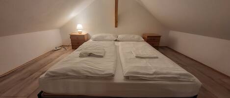 Un lit simple avec une tête de lit en bois, dans une pièce dont le plafond est en pente.