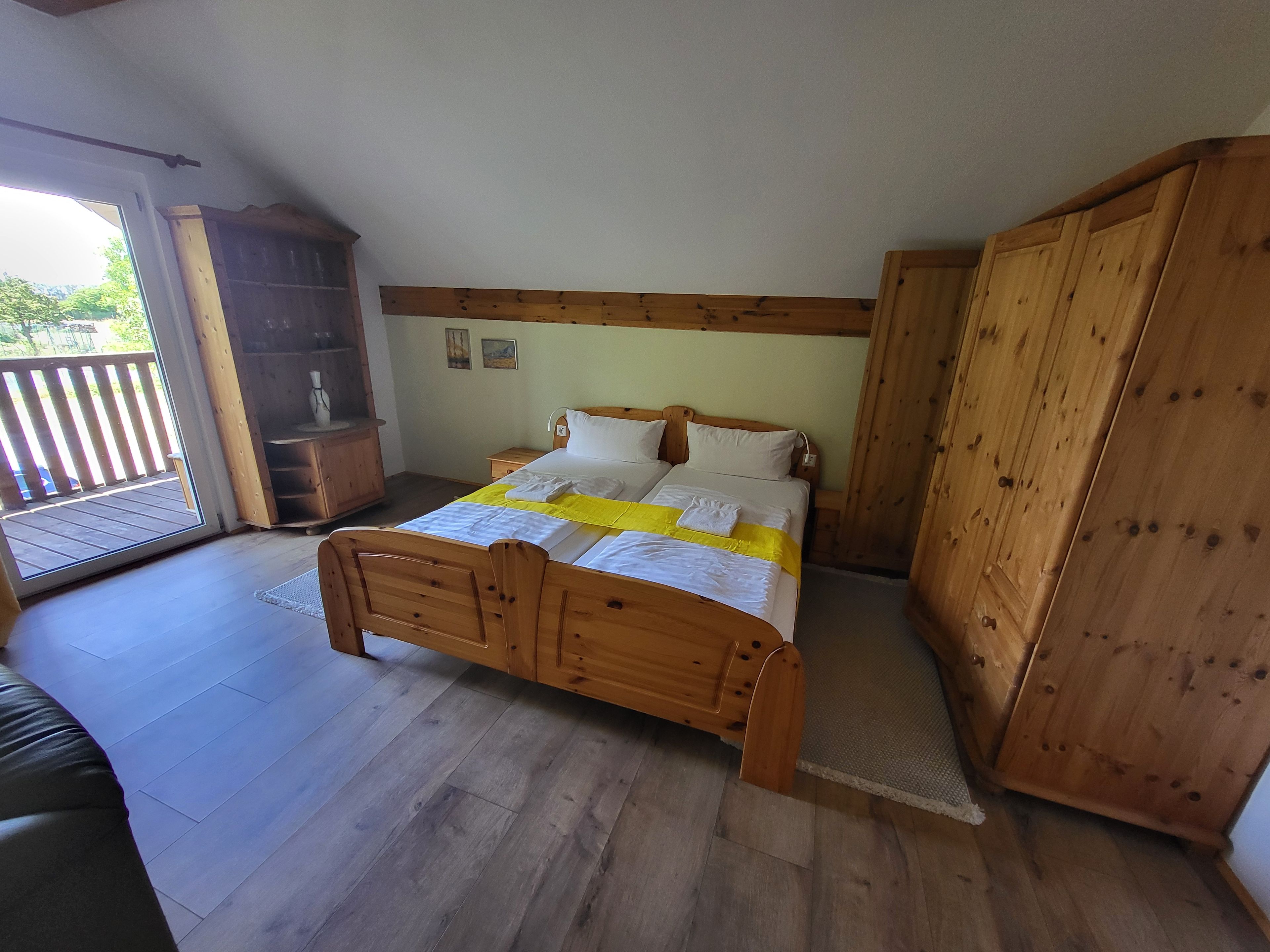 A bedroom with a wooden bed, a wardrobe, and a view of the outdoors.