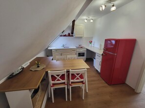 A compact kitchen with a wooden table, white chairs, a red refrigerator, and a small countertop.