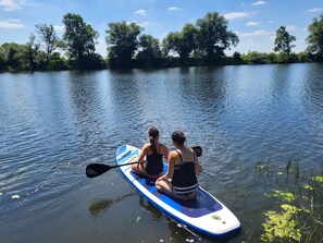 Two people sitting on a paddleboard in a calm body of water with trees in the background. - Modern vacation rental on a country estate with a large garden, plenty of nature, a courtyard garden, and a lake (Kehnert)