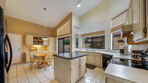 A modern kitchen with a central island, white cabinetry, and a dining area with wooden chairs.