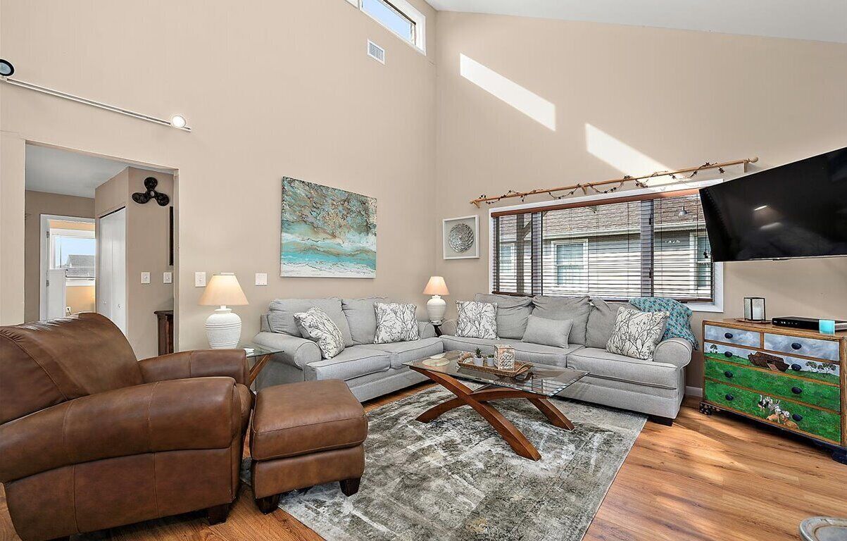 Un salón espacioso con un sofá modular, un sillón de cuero marrón, una mesa de centro y un televisor sobre un mueble.