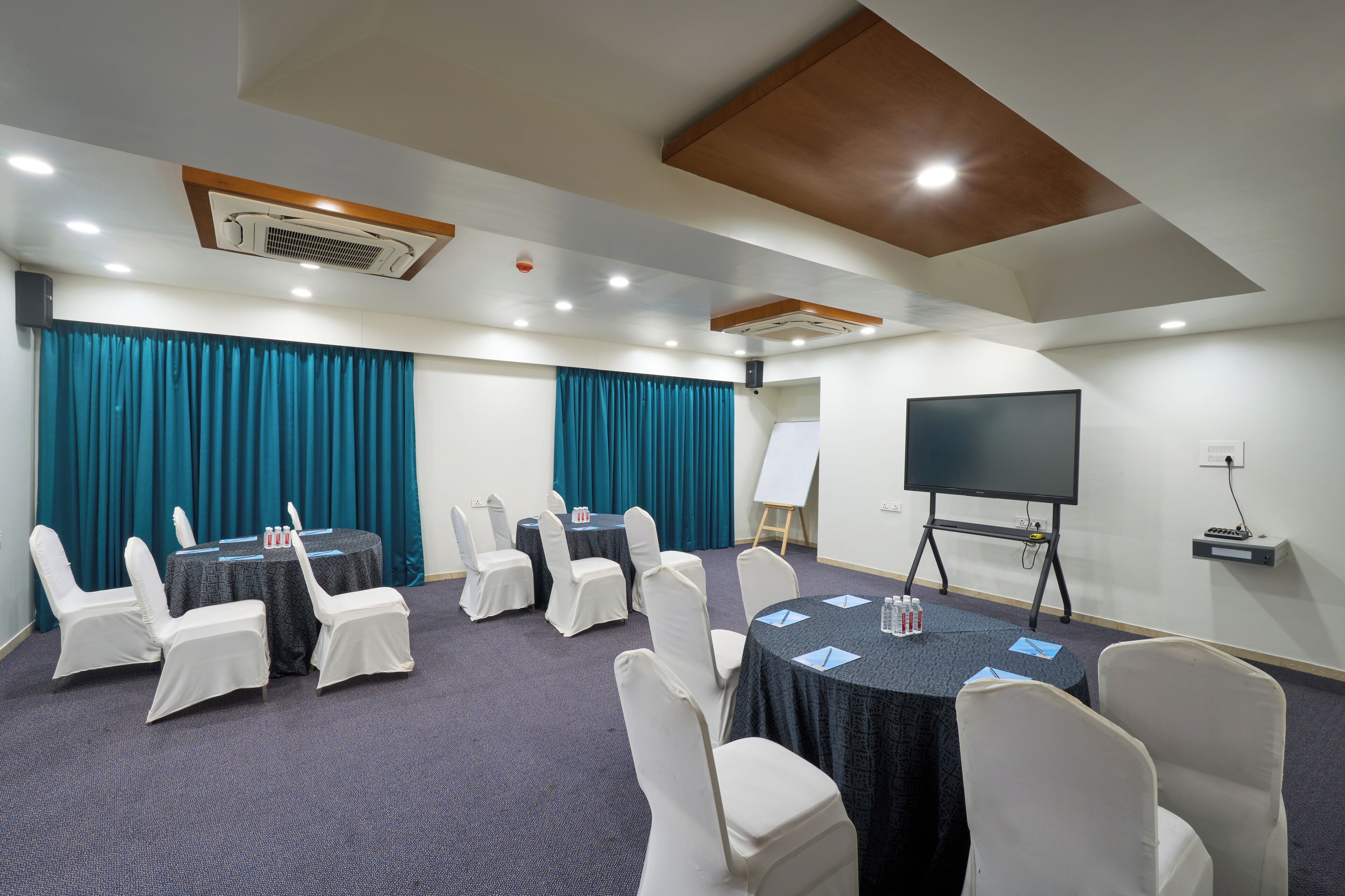 Uma sala de conferências com mesas, cadeiras, um projetor e uma tela.