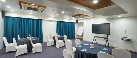 Una sala de conferencias con mesas, sillas, un proyector y una pantalla.