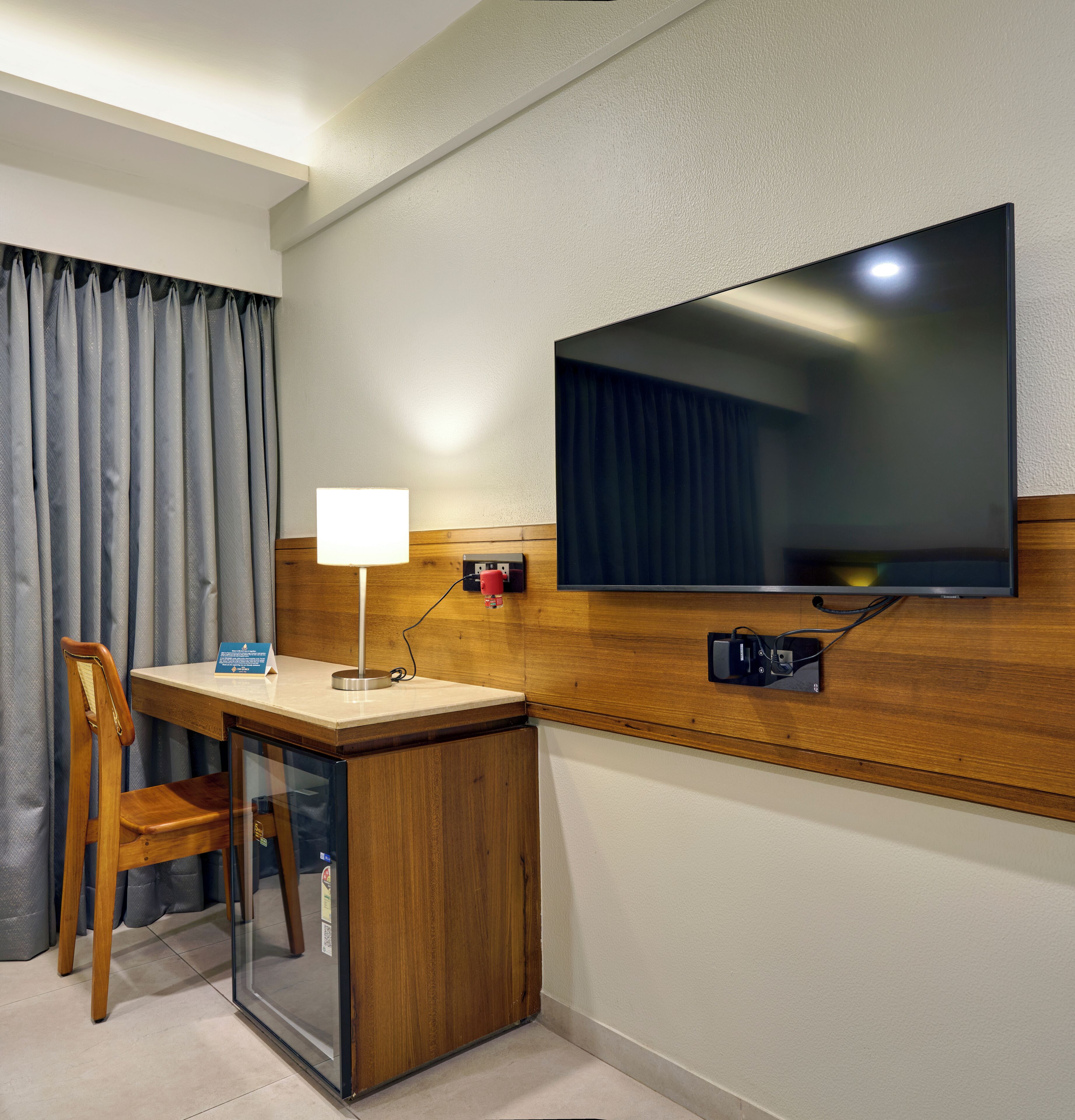 Een hotelkamer met een houten bureau, een stoel, een aan de muur bevestigde televisie en een lamp.