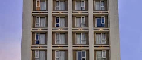 Un hotel de varios pisos con fachada plana, numerosas ventanas y entrada a nivel de calle con estacionamiento para automóviles.
