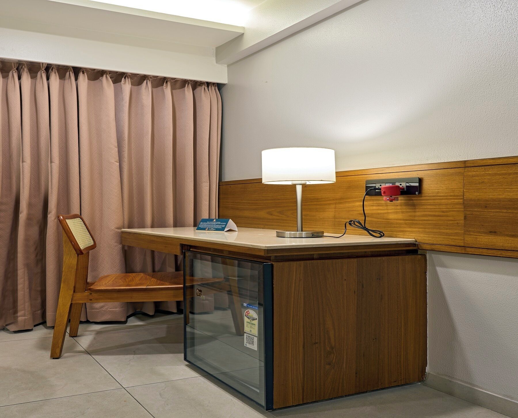 Une chambre d’hôtel équipée d’un bureau, d’une chaise, d’une lampe et d’un mini-bar.