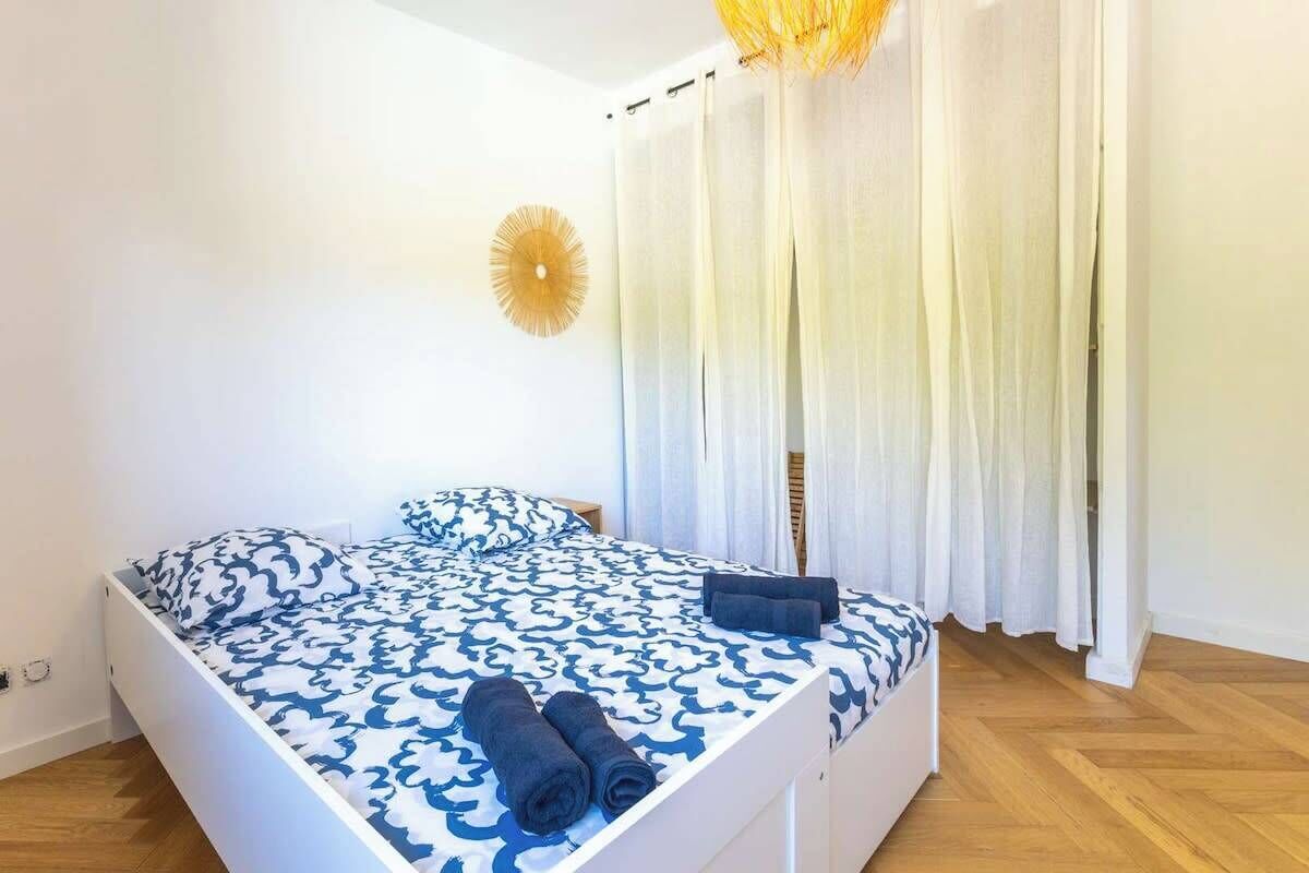 A bedroom with a bed, white walls, a wooden floor, and a ceiling light fixture.