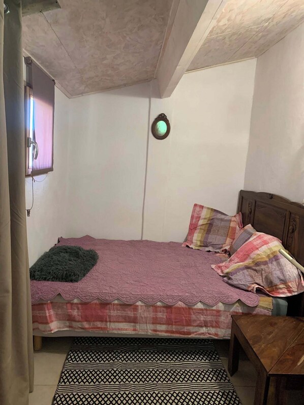 Ein kleines, gemütliches Schlafzimmer mit einem Einzelbett, einem Nachttisch aus Holz und einer Wandleuchte.