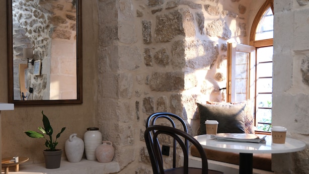 A stone-walled room with a round table, chairs, a potted plant, and a window with a view. - Kaia House (Mardin)