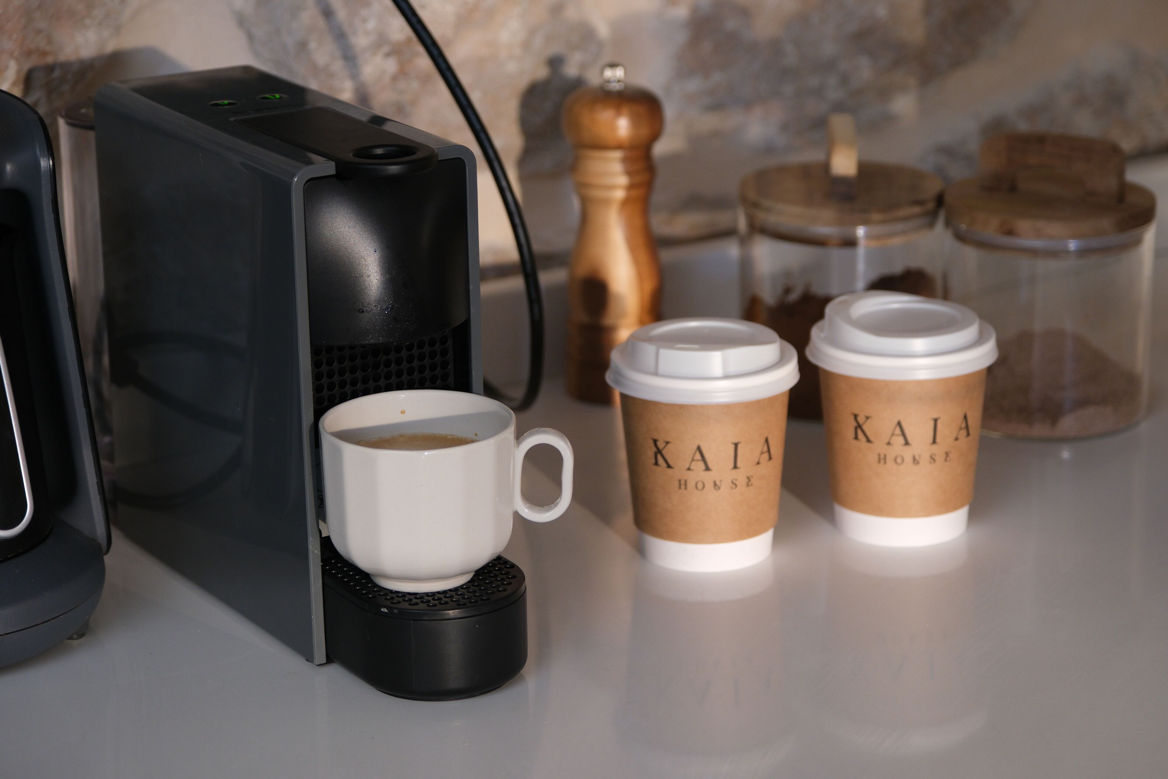 Eine Kaffeemaschine, zwei Kaffeetassen, ein Gewürzmühle und Gläser auf einer Arbeitsplatte.