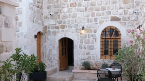 A stone courtyard with a wooden door, a small table with chairs, and potted plants. - Kaia House (Mardin)