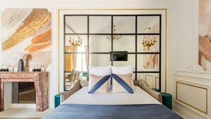 A bedroom with a large bed, a desk with a vase, and a wall with a painting. - Merveil Luxury Suites - Bac I-II (Paris)