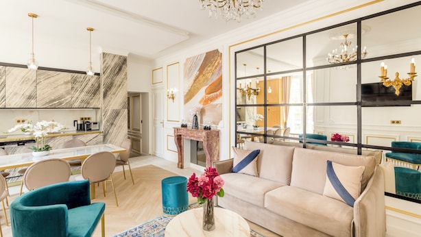 A modern living room with a beige sofa, teal armchairs, a coffee table, and a large mirror. - Merveil Luxury Suites - Bac I-II (Paris)