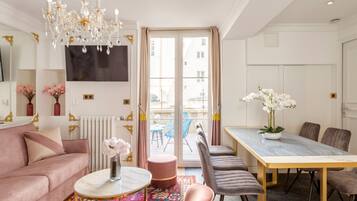 Een moderne woonkamer met een roze bank, een ronde salontafel, een kroonluchter, en een eethoek met een tafel en stoelen.
