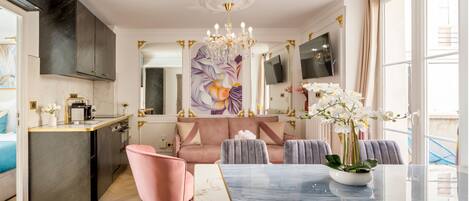A modern kitchen with a marble countertop, a pink chair, a dining table with a vase of flowers, and a large painting on the wall.