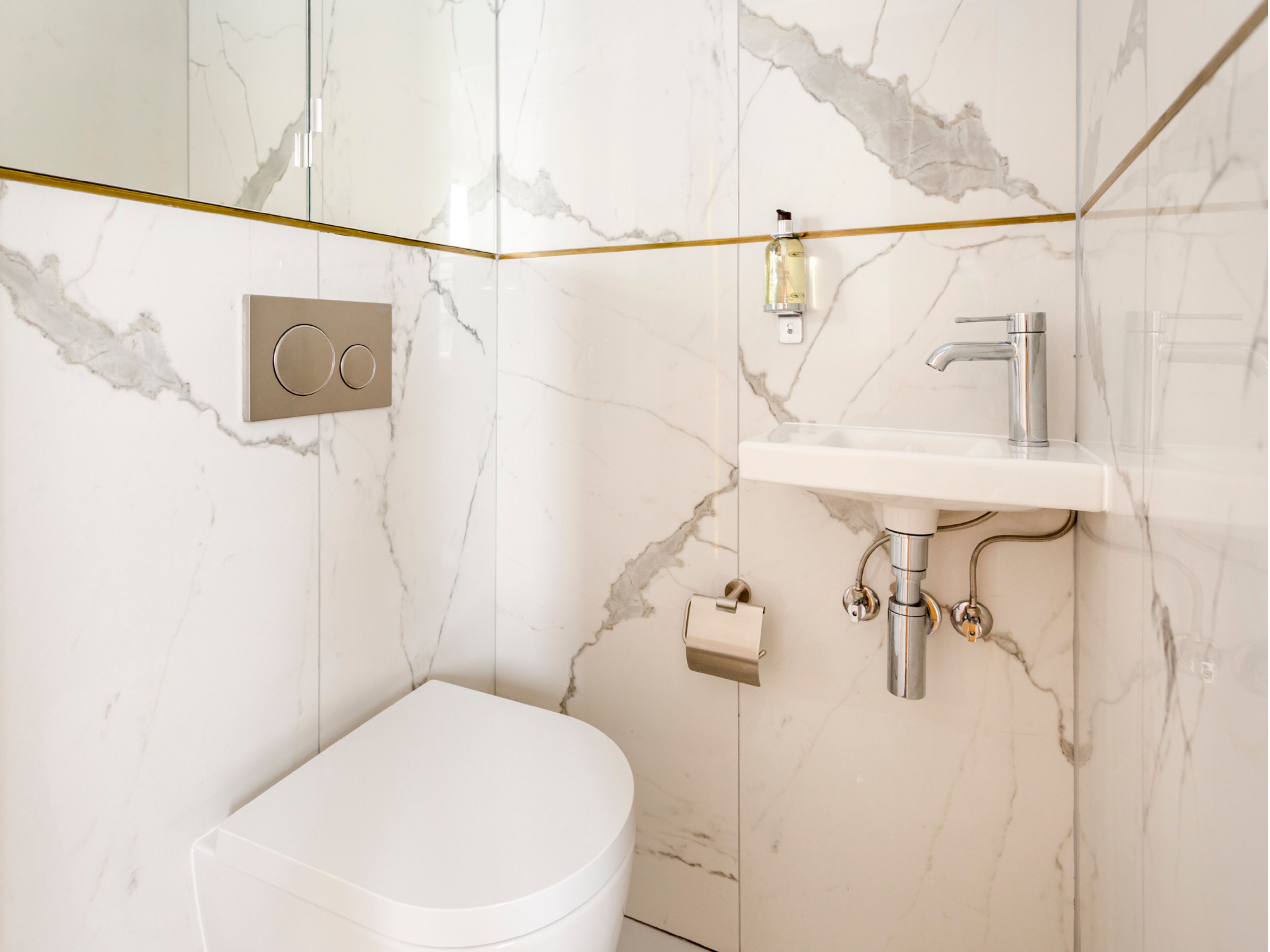 Een badkamer met een wit toilet, een wastafel met een kraan en een marmeren wand.