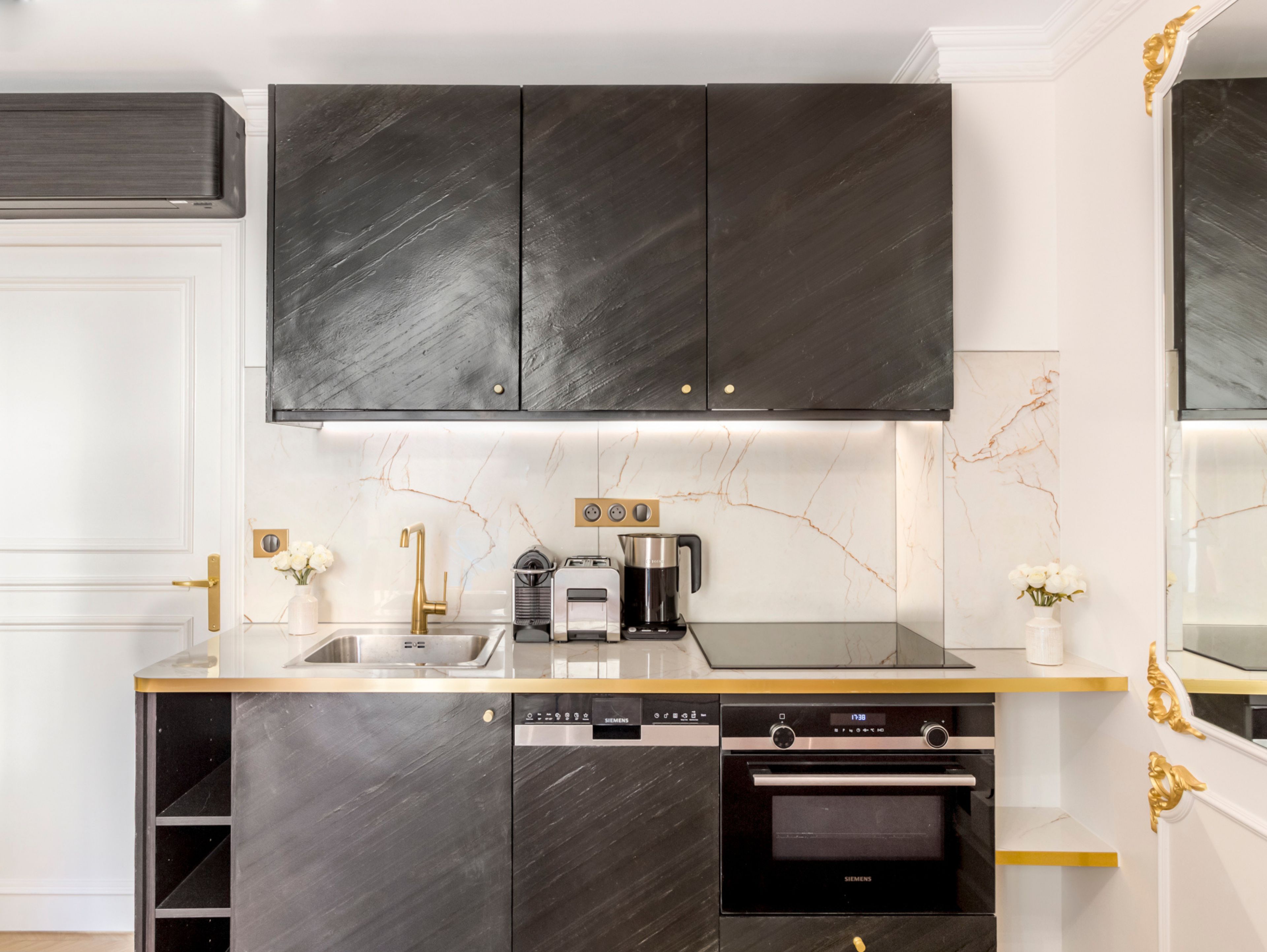 A modern kitchen with dark cabinets, a marble backsplash, and stainless steel appliances including a dishwasher, oven, and coffee maker.
