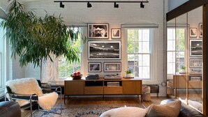 A spacious living room with a large window, a wooden console table, a leather sofa, and a hanging plant.