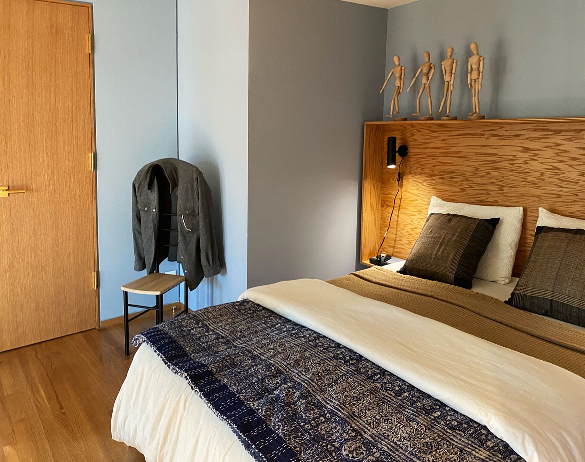 Een slaapkamer met een houten hoofdbord, een bed met beddengoed met een patroon, een klein tafeltje met een jas en een deur.