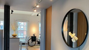A modern interior with a wooden dining table, chairs, a round mirror, and a potted plant.