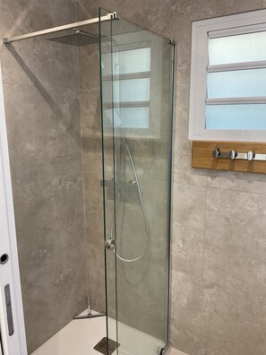 A glass-enclosed shower stall with a chrome showerhead and control panel, adjacent to a wooden cabinet with a window above.