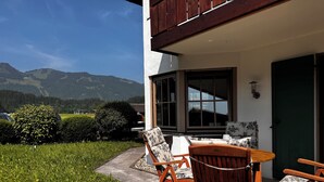 A patio with a table and chairs, a view of mountains, and a building with a green door.