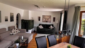 A living room with a sofa, a coffee table, a dining table with chairs, a fireplace, and a painting on the wall.
