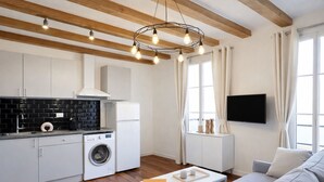 A modern kitchen with a washing machine, a dining area with a table and sofa, and a TV mounted on the wall. - 1579 StDominique3 (Paris)