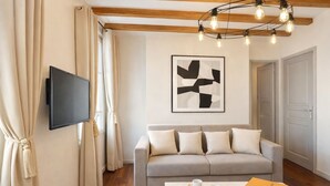 A modern living room with a sofa, a flat-screen TV, a coffee table with a tray, and a Louis Vuitton box. - 1579 StDominique3 (Paris)