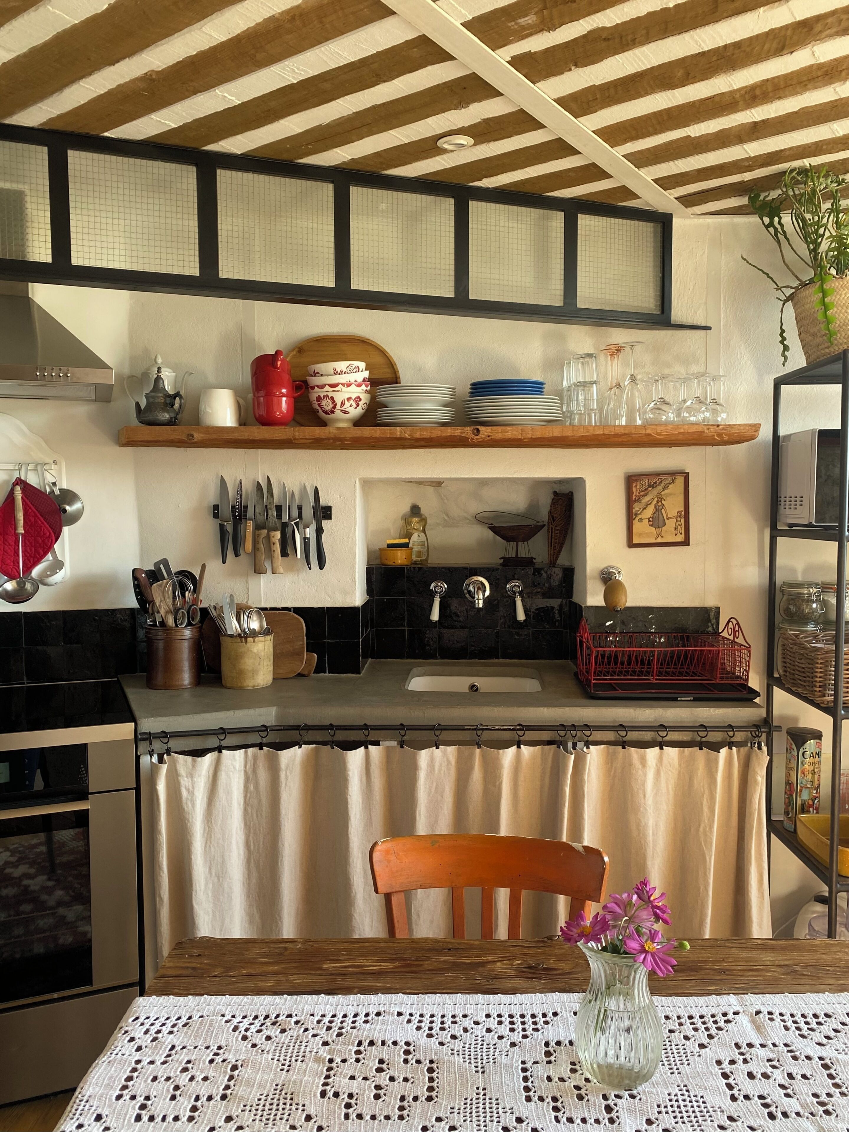 A kitchen with wooden shelves, a sink, and a dining table with a lace tablecloth.