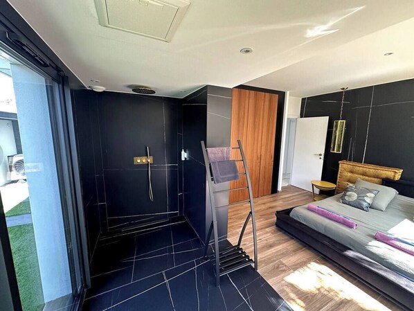 A modern bedroom with a large bed, a wooden headboard, and a black tiled shower area.
