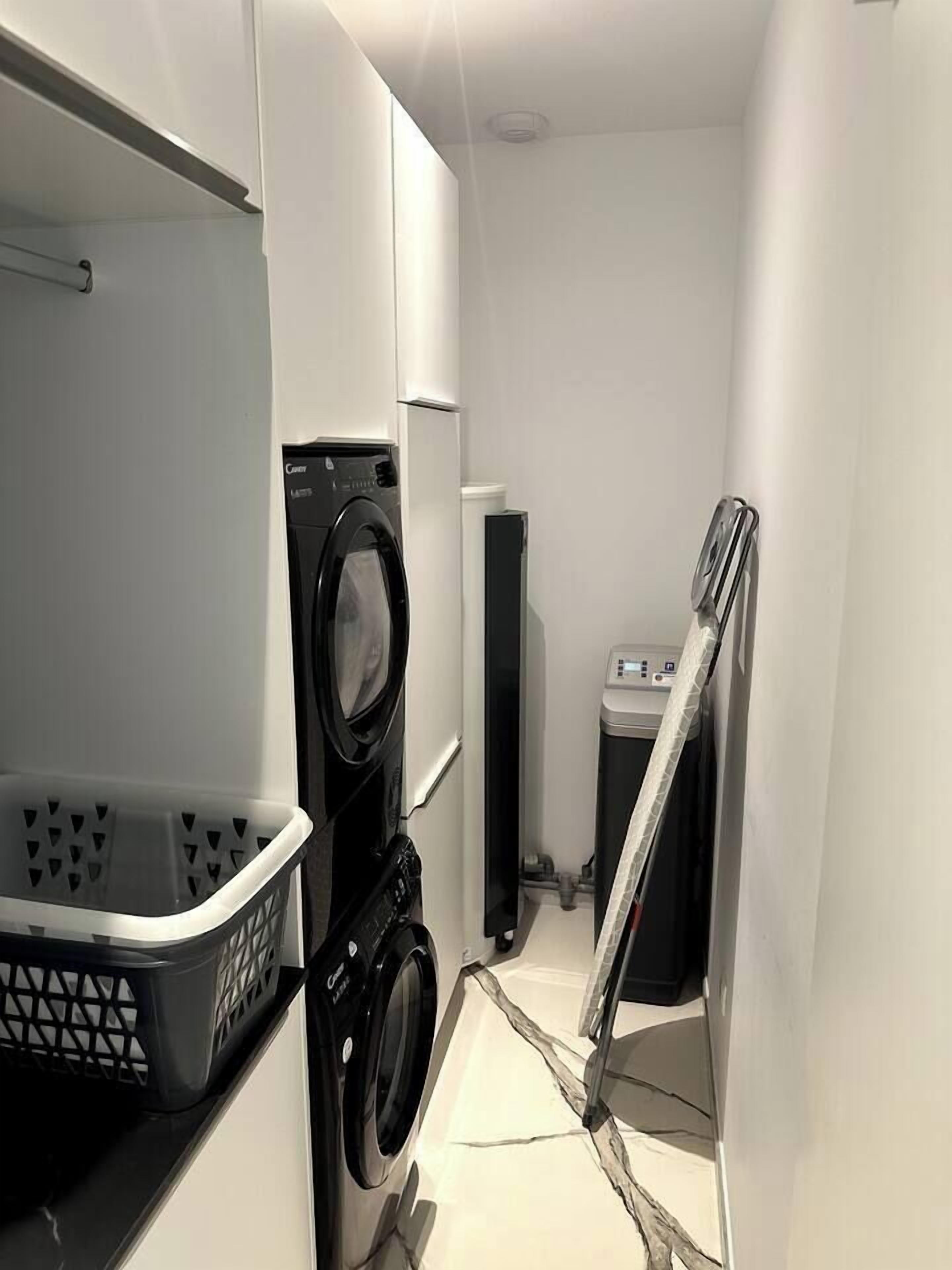 Een kleine wasruimte met een voorlader wasmachine, een droger en een klein berghok met een boiler.