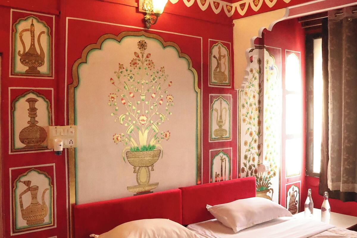 Una habitación con una cama, un ventilador de techo y una pared decorada con arte tradicional.